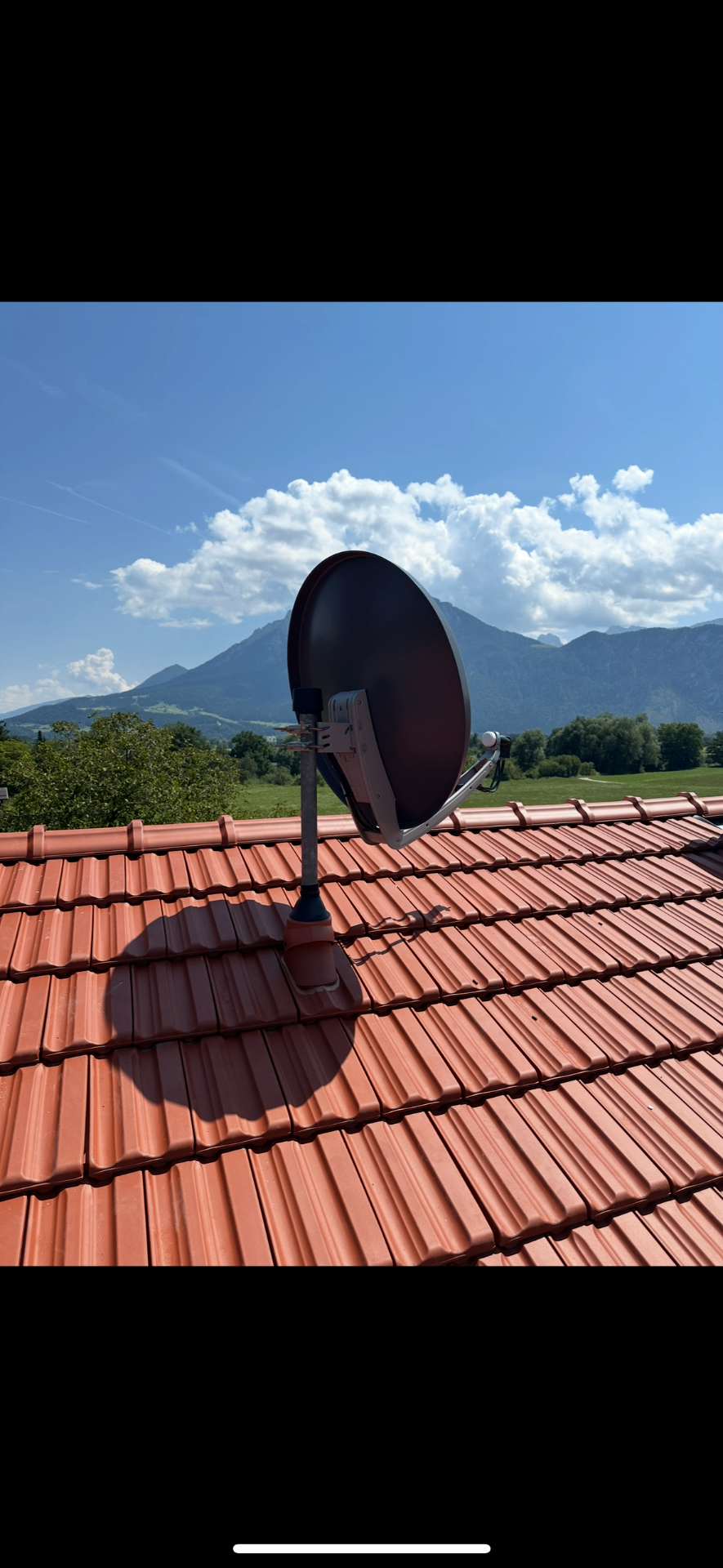 SAT-Anlage auf rotem Ziegeldach vor Bergpanorama